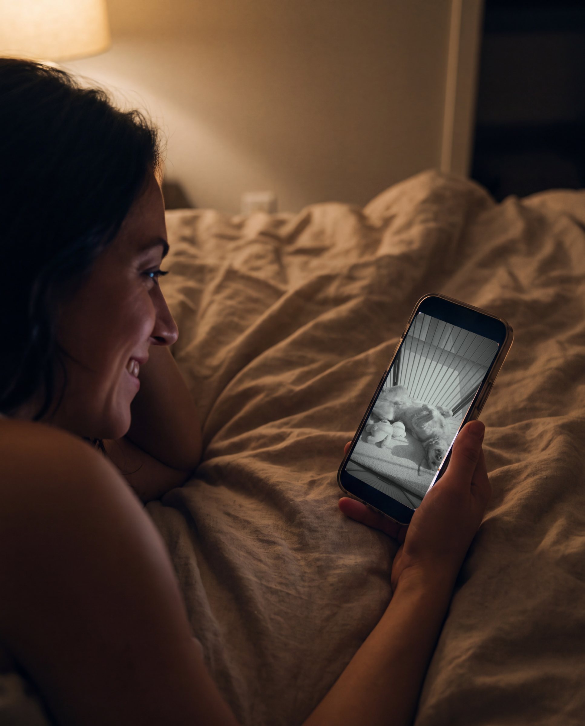 Late at night in bed, a woman checks the night-vision live view of her dog asleep in Koja